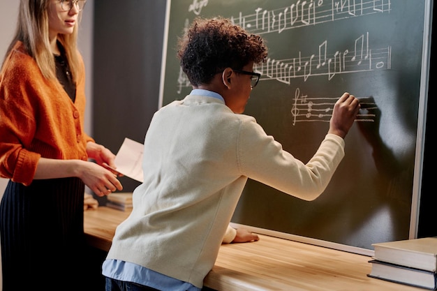 Photo un garçon afro-américain écrivant des notes de musique sur un tableau noir.