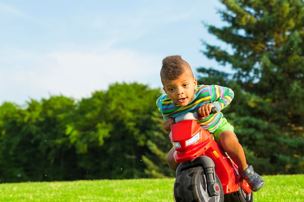 Garçon afro mignon sur le jouet de moto rouge.