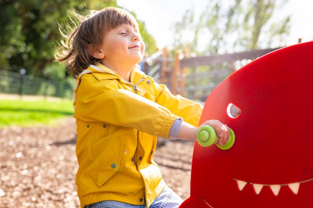 Garçon d'âge préscolaire sur l'aire de jeux pour enfants heureux enfant émotionnel se balançant sur la bascule dans un parc Concept de l'enfance