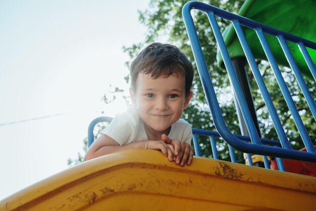 Photo un garçon d'âge préscolaire heureux jouant sur une glissière sur le terrain de jeu en été