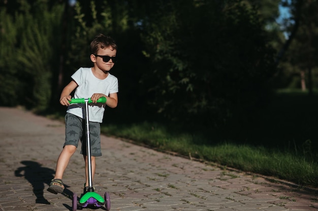 un garçon d'âge préscolaire monte un scooter dans le parc en été