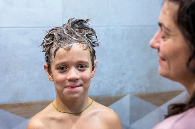 Un garçon d'âge préscolaire se lave la tête dans la salle de bain avec du shampoing