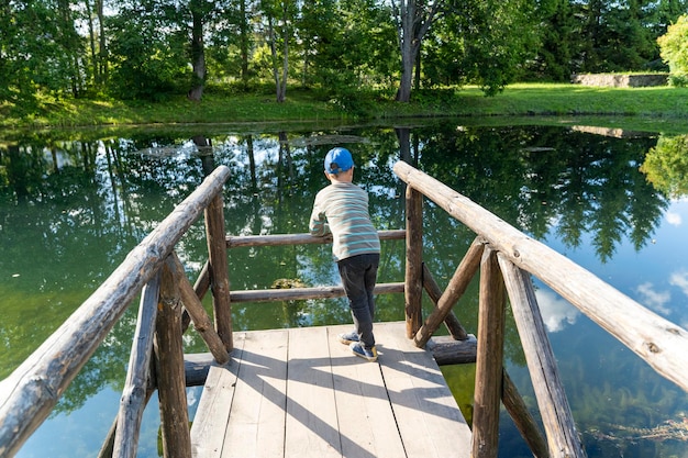 Le garçon d'âge préscolaire se repose s'appuyant sur les ponts en bois de l'étang