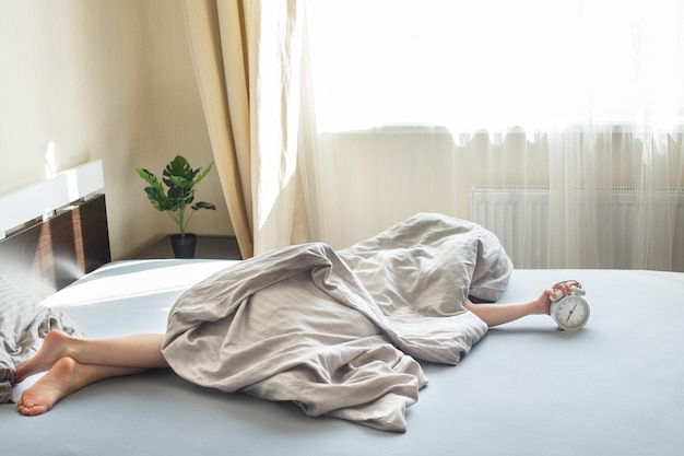 Garçon allongé sur le lit sous une couverture et arrêtant le réveil le matin