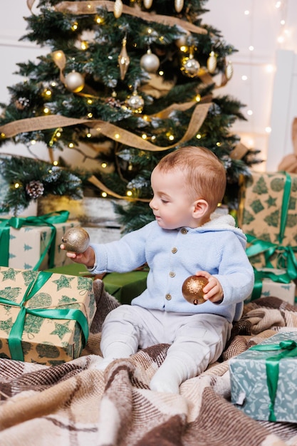 Photo un garçon d'un an est assis près d'un arbre de noël décoré avec des cadeaux arbre de noël dans la maison un enfant heureux attend la nouvelle année