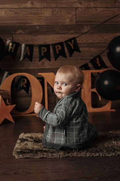 Un garçon d'anniversaire dans un costume gris s'assied avec son dos sur un fond de fête