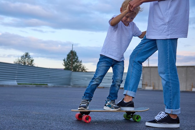 Un garçon apprend à un enfant à faire du skateboard l'aide à monter sur un skateboard