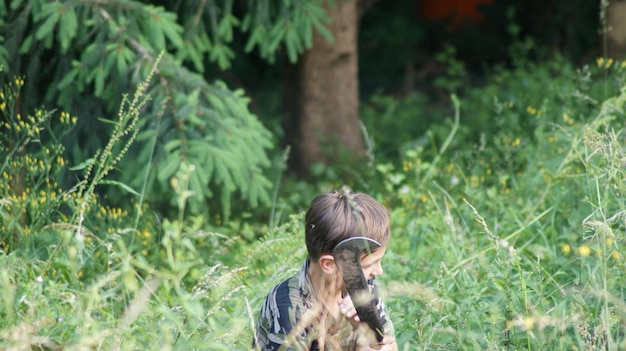 Photo un garçon avec une arme assis au milieu des plantes