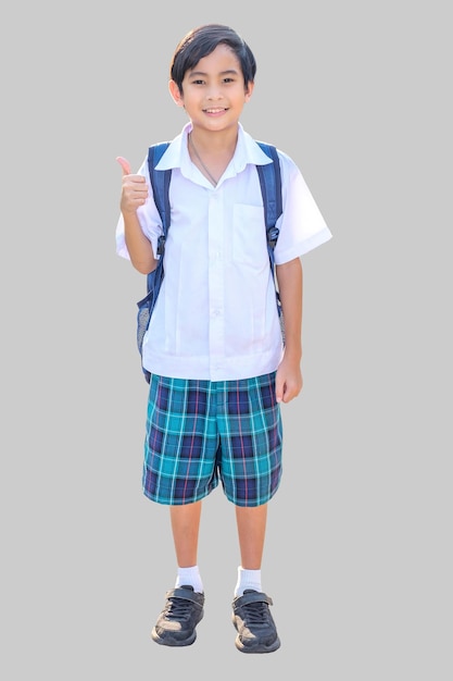 Un garçon asiatique de 10 ans en uniforme scolaire se tient debout avec les mains levées les pouces en l'air et sourit