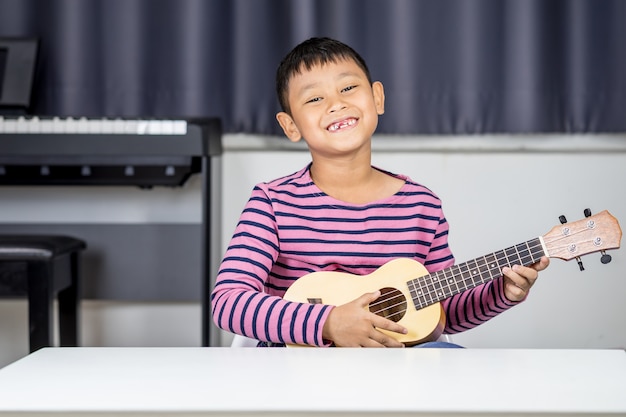 Garçon asiatique âgé de 7 à 8 ans: ukulélé dans la chambre, amour passionné en musique