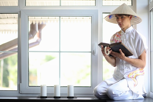 Garçon asiatique en kimono lisant un vieux livre assis près de la fenêtre