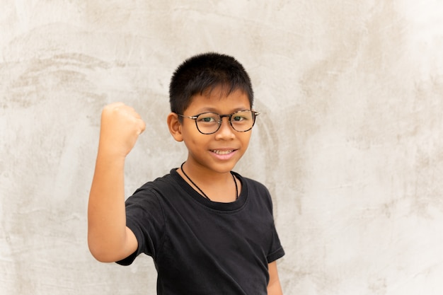 Garçon asiatique avec des lunettes mains et souriant sur fond gris.