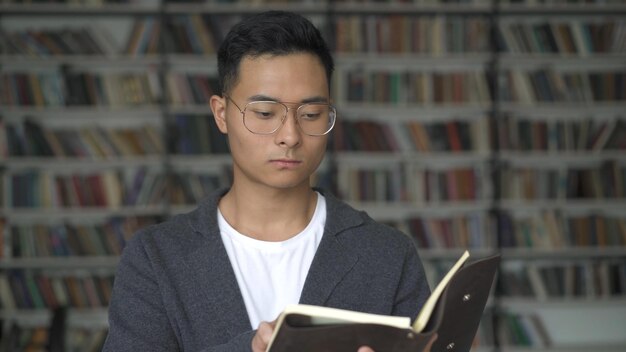 Garçon asiatique avec des lunettes tenant un livre sur fond d'étagères