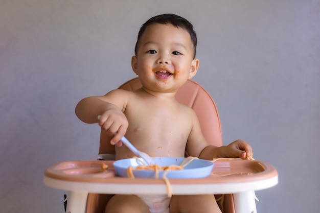 Garçon asiatique, manger sur une chaise haute pour bébé