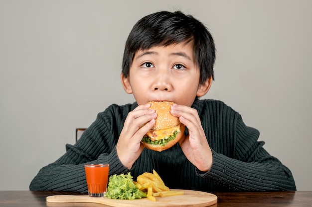 Garçon asiatique mignon mangeant un délicieux hamburger avec bonheur