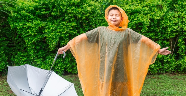 Garçon asiatique portant un imperméable orange tenant un parapluie heureux et s'amusant sous la pluie un jour de pluie