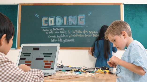 Un garçon asiatique programme de codage pendant qu'un ami répare un tableau électrique en classe de pédagogie