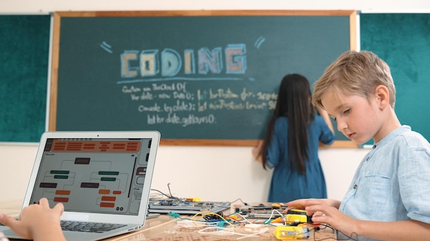Un garçon asiatique programme de codage pendant qu'un ami répare un tableau électrique en classe de pédagogie
