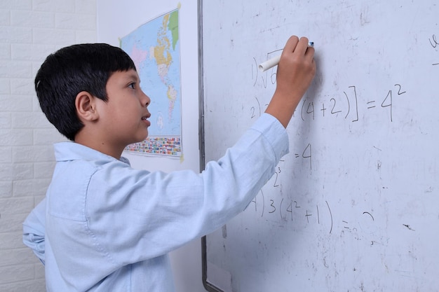 Garçon asiatique solution d'écriture de racine carrée sur tableau blanc à l'école