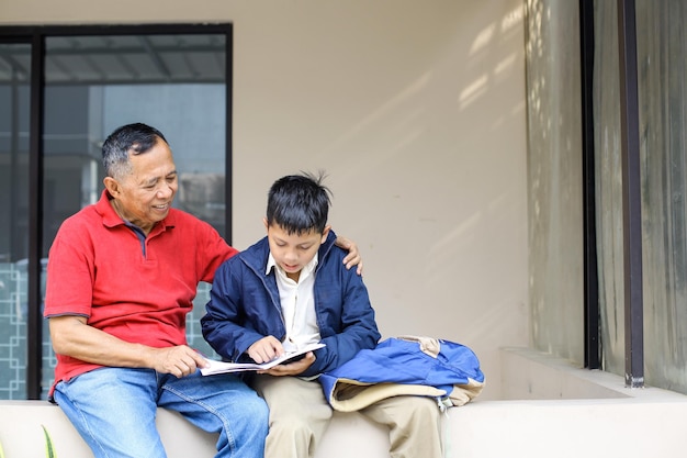 Un garçon asiatique en uniforme apprend sérieusement avec son grand-père dans la cour de la maison Grand-père enseigne gra