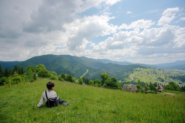 Un garçon assis au sommet de la colline et regardant les montagnes