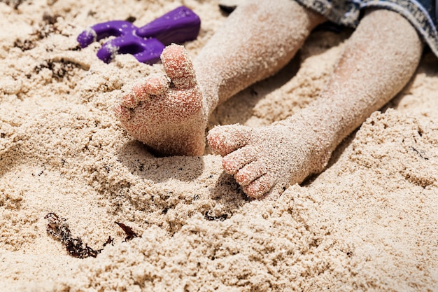 Garçon assis aux pieds nus sur la plage de sable fin, vacances d'été