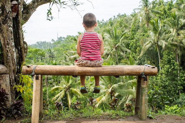 Garçon assis sur le banc sur fond de montagnes à Ubud Bali