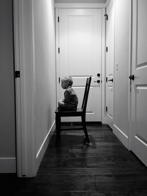 Photo un garçon assis sur une chaise en bois dans le couloir