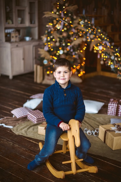 Garçon assis sur le cheval en bois en face de l'arbre de Noël