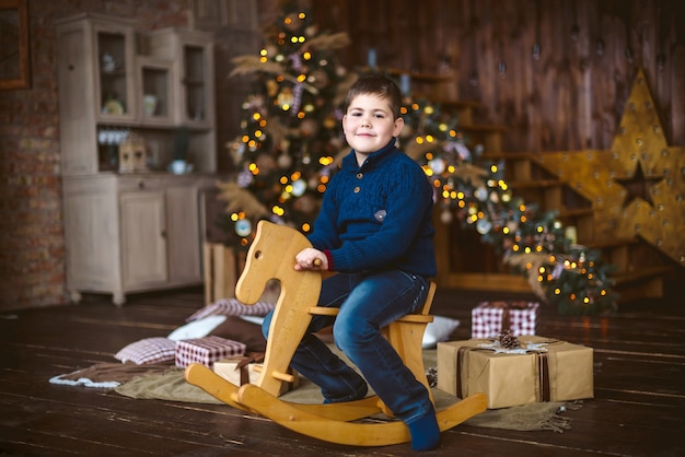 Garçon assis sur le cheval en bois en face de l'arbre de Noël