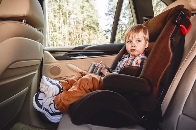 Garçon assis dans une voiture dans une chaise de sécurité road trip en famille