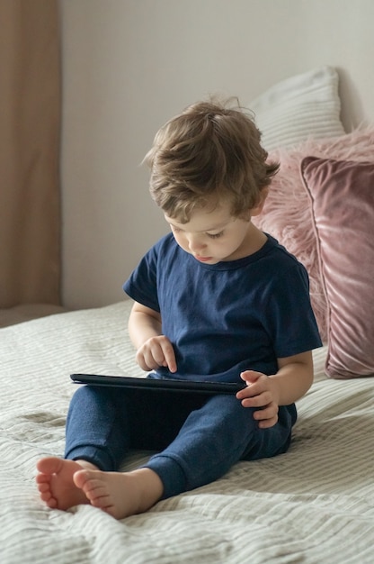 Garçon assis avec une tablette sur le lit