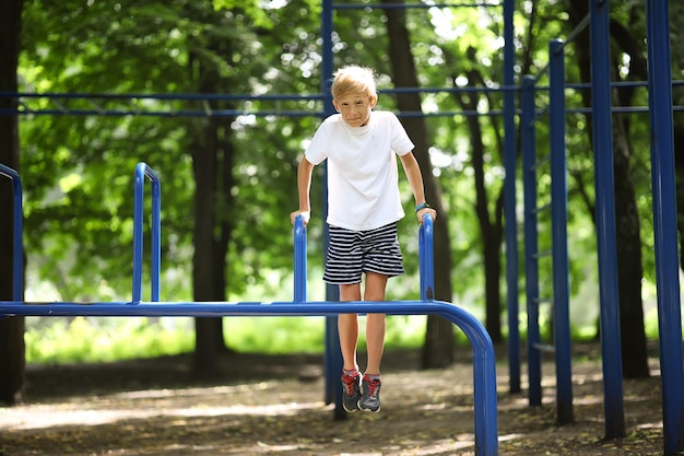 Garçon athlète dans le parc accroché à ses mains et fait des exercices sur les barres asymétriques