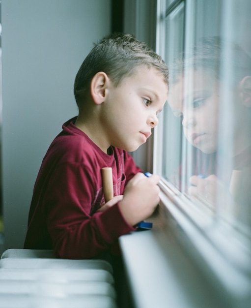 Un garçon attentionné qui regarde par la fenêtre à la maison.