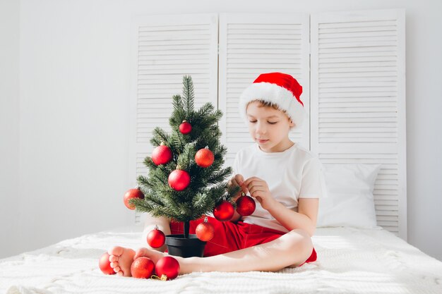 Garçon au bonnet rouge décore une petite boules de sapin