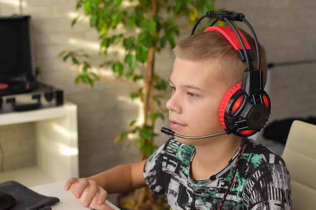 Un garçon au casque est assis devant un ordinateur et joue à un jeu. dépendance aux gadgets de jeux pour enfants