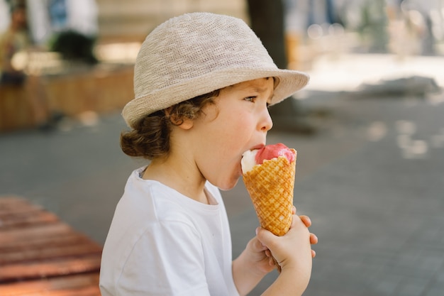 Un garçon au chapeau tient une glace et a l'air heureux et surpris de la nourriture estivale et de l'heure d'été