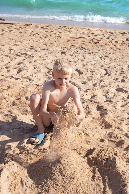 Un garçon aux cheveux blonds joue avec du sable en le jetant Aventure au bord de la mer un jour d'été