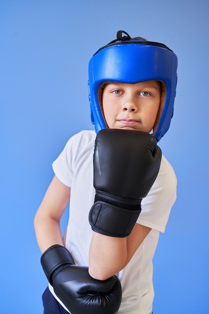 Un garçon aux yeux verts portant un casque de boxe et des gants sur fond bleu