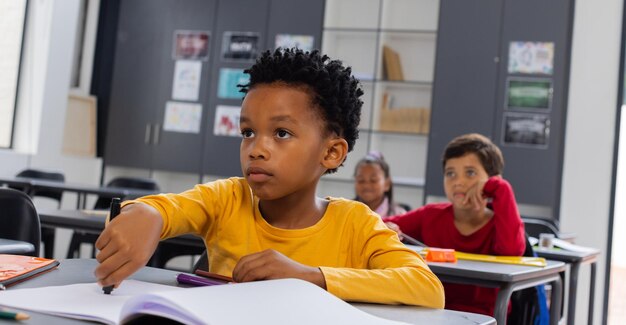 Photo un garçon biracial en chemise jaune a l'air attentif dans une salle de classe.