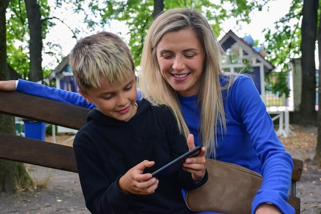 Un garçon blanc attrayant et sa belle maman regardent un téléphone portable et sourient joyeusement