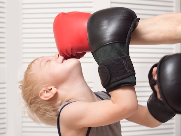 Garçon blond boxe avec la main dans le gant rouge. Coup au visage