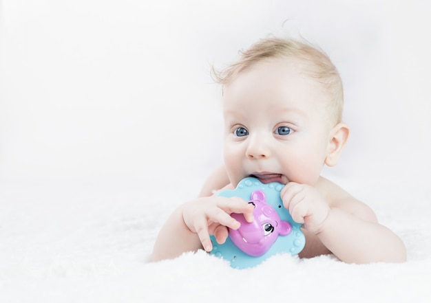 Photo garçon blond de cinq mois aux yeux bleus se trouve sur le ventre avec un jouet dans ses mains