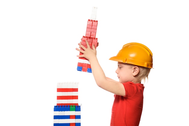 Un garçon blond dans un casque de construction construit un gratte-ciel à partir des détails du concepteur.