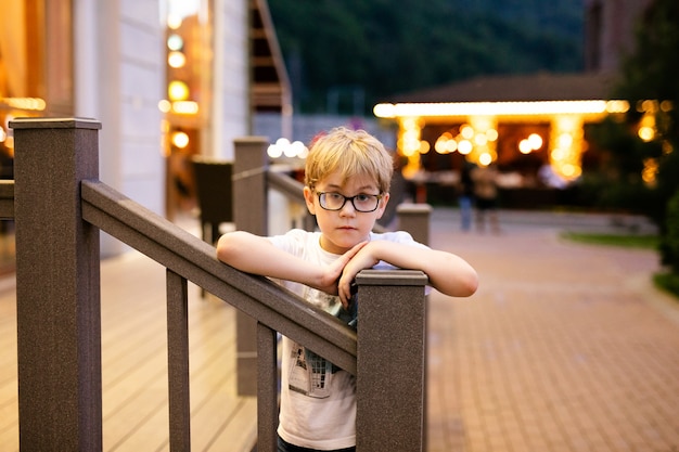 Garçon blond dans les grandes lunettes marchant dehors le soir