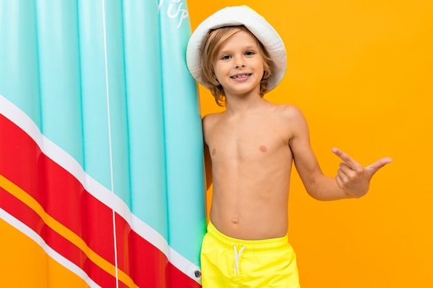 Garçon blond dans un panama d'été avec une planche de natation gonflable sur jaune