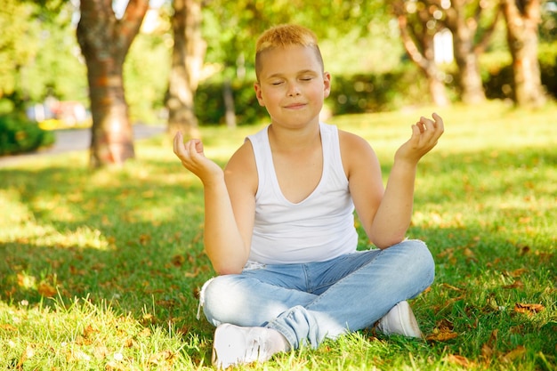 Garçon blond dans un t-shirt blanc est assis sur l'herbe dans le parc