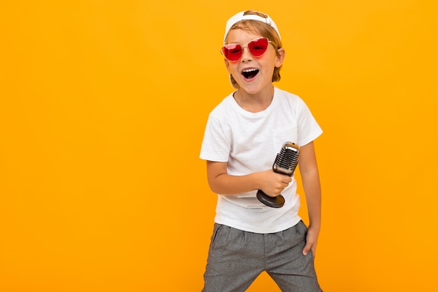 Garçon blond à lunettes chante dans un microphone sur fond jaune