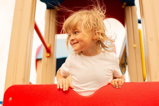 le garçon blond regarde au loin debout sur le toboggan de l'aire de jeux