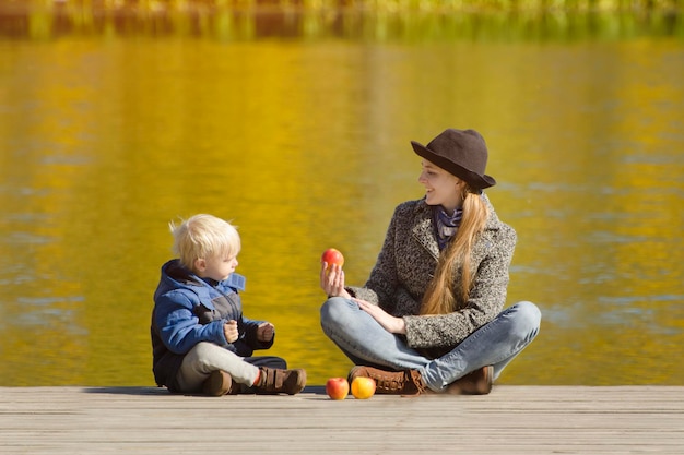 Garçon blond avec sa mère assise sur la jetée et jouant avec des pommes Journée d'automne ensoleillée